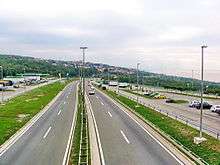 Six-lane motorway route passing through a rest area, with parking areas on both sides of the route and a filling station.