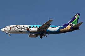 Right side view of a Boeing 737 with a livery of sled dogs pulling a canoe and beluga whale, against a blue sky