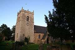 Church with substantial tower under a sky of duck-egg blue, with a large Yew on the right., a very dark green.  The tower is broad, but barely higher than the deeply pitched roof on the nave.  It has a clockface on the nearest side.