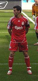 Man in red shirt standing with his arms behind his back.