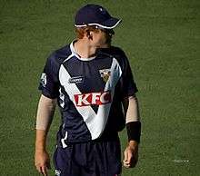 An Australian cricketer wearing blue-white outfit and looking to his left.