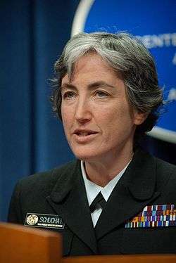 A woman with silver-colored hair in a military uniform looking left with her mouth slightly agape