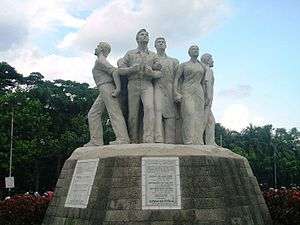 Four figures stand in a circle holding up the symbol of Wikipedia, which consists of a globe made of jigsaw pieces, with few pieces missing, symbolizing that the work of the encyclopedia will never be finished