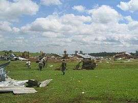 A destroyed poultry farm with debris strewn across a field