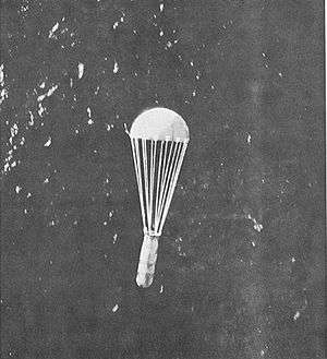 A parachute with a canister hanging below it dropping over the sea