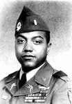 Head and shoulders of a black man with full cheeks in military uniform. Rows of ribbon bars are on his left breast and his lapels and garrison cap are adorned with pins and badges.