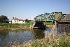 Rivetted steel railway-era carries a narrow road over the river Welland into the town from the west