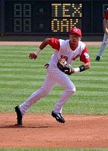 A man in a white baseball uniform with red pinstripes and a red baseball cap running to his left