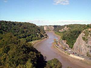 River flowing through gorge with wooded sides. On the right hand bank is a road