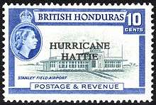 A rectangular postage stamp, denoting that the stamp is of the British Honduras and costs ten cents. In the center there is a picture of the terminal to Stanley Field Airport, with the words 'HURRICANE HATTIE' printed over it. At the bottom of the stamp reads 'Postage & Revenue'.