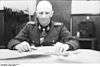 A man stiing at a desk, wearing a military uniform and neck order, in the shape of a cross.