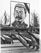 A man with dark hair and moustache, wearing a uniform, posted over a military parade