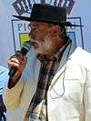 Man in traditional huaso dressing, wearing a hat and a white jacket, holding a microphone