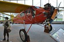 Small airplane with single wing over top; single wooden propeller in front; "Newsboy" painted on fuselage