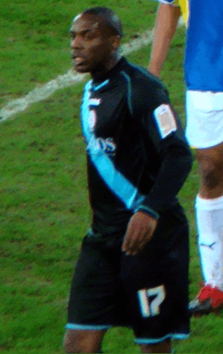 Young shaven-headed black man wearing black kit participating in a sporting encounter.