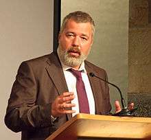 A man with a full beard, Dmitry Muratov, speaking at a podium