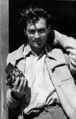 A photo of Ernst Haas leaning in a doorway, holding a camera in his right hand.