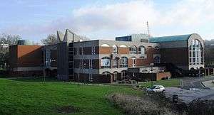 A long, low brick and concrete building with a large curved-roofed wing to the right