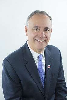 Felix V. Matos Rodriguez, smiling, with a high hairline of grey hair, wearing a dark suite jacket and a blue tie, sitting turned forty-five degrees from the camera against a neutral pale background