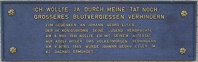 A plaque with the German text in all capital letters:'"Ich wollte ja durch meine Tat noch größeres Blutvergießen verhindern." Zum Gedenken an Johann Georg Elser, der in Königsbronn seine Jugend verbrachte. Am 8. Nov. 1939 wollte er mit seinem Attentat auf Adolf Hitler das Völkermorden verhindern. Am 9. April 1945 wurde Johan Georg Elser im KZ Dachau ermordet.'