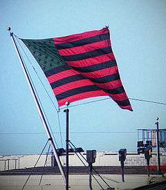 The flagstaff is set atop the building, tilted 45° to the left, and the flag is rippling in the wind to the right.