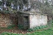 Small brick shed with a door and concrete roof, built up against an ironstone quarry face.