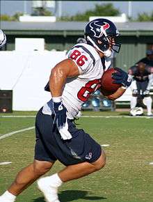  An football player running from left to right on a football field. He is wearing a red, blue and white uniform