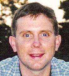 A headshot of a man with short brown hair, blue eyes and light skin with an excited expression on his face looking directly at the camera