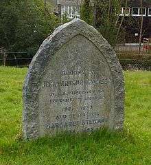 A granite headstone, pointed like a Gothic arch, in a grassy churchyard