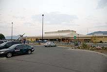 A local parking lot with a number of automobiles using the service; there is also a building of an airport, which contains its terminal.