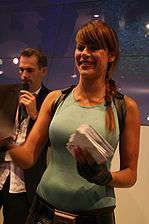 A half body picture of a brunette woman dressed in a light blue, sleeveless shirt holding a stack of papers.