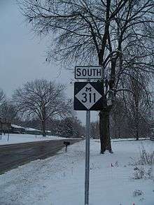 A highway sign alongside the road on a snowy day.