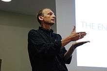 Photograph of Felleisen standing in front of a projector screen, gesturing