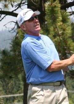 Mike Schmidt watches a ball while golfing with pine trees in the background