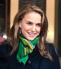 An image of a smiling woman with light brown hair in her 20s. She is wearing a tucked in green scarf with a dark colored coat.
