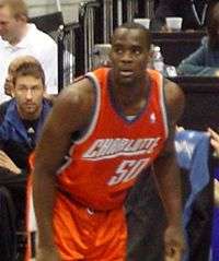 A black person wearing an orange-color jersey stands in front of the spectators