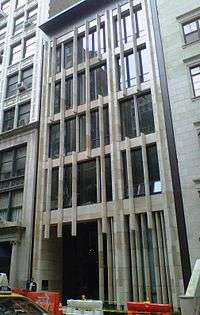 The narrow, six-story facade of a building has white poles going vertically all along its facade.