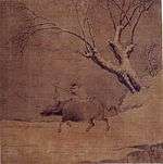 A boy riding an ox and a tree.