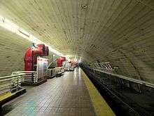 a long barrel vaulted room with red pipes emerging from the center of the floor and train tracks on the right