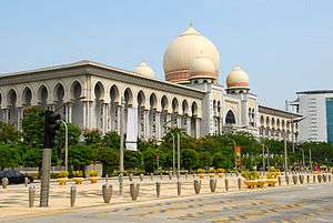 Building taken from a view of the corner. Beige colour, surrounded by columns. A large dome can be seen on the roof, surrounded by 3 others