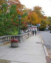 A walkway between a road and autumn trees