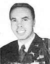 Head of a smiling young man with dark hair wearing a military jacket with pins on the lapel over a shirt and tie.