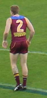 A man in a maroon football jersey wearing number 2 stands on grass.