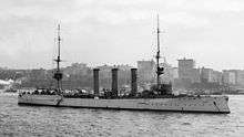 A large ship at anchor in harbor, with a line of buildings in the background