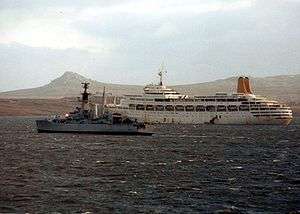 Small grey ship and larger white ship, with mountain in background