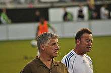 Two men with a footballer warming up behind them