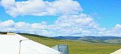 Puffy white clouds roll over lush green hills.