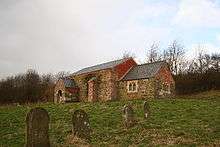 Seen from a distance, in a graveyard, is a simple stone church, the chancel smaller and lower than the nave; protruding from the wall are a buttress and a porch