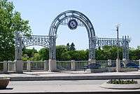 A cast iron triple arch about four metres in height and painted white. The words "Progress" and "Prosperity" can be seen above the left and right arches respectively.