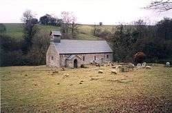 A simple single-storey church seen from a distance with a bellcote and a porch; sheep graze in front of it